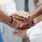 healthcare providers with stacked hands representing a positive healthcare workplace